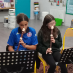 Students sitting in chairs, playing recorders with their noses