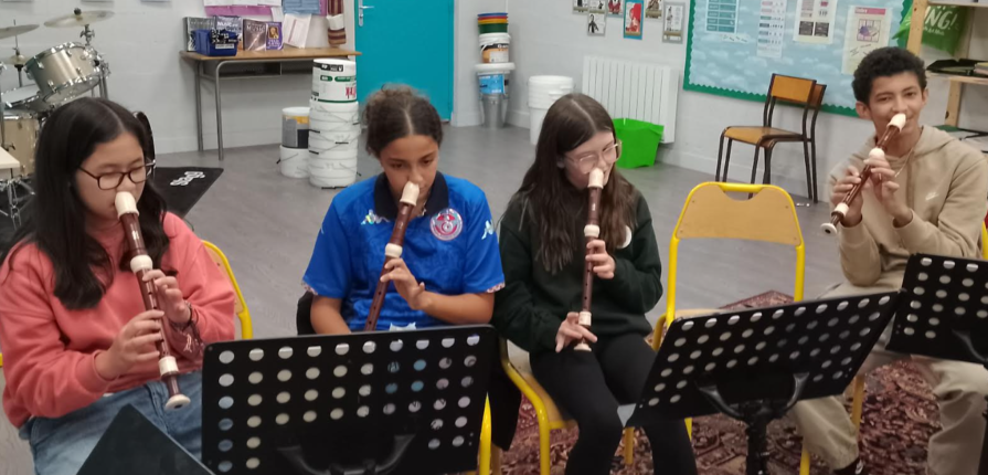 Students sitting in chairs, playing recorders with their noses