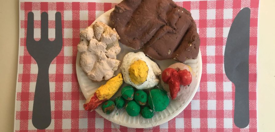 A plate with some foods made out of play dough (egg, bread, peas, etc.)